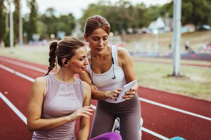 shutterstock_2554610065 Two women at a running track looking at a tablet