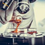 Archaeologists Discover 3,000 Year Old Honey – Still Edible! Gloved hand pouring orange liquid into a petri dish under a microscope