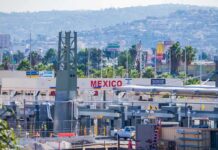 Consumer Panic: Avocado Pipeline Suddenly Freezes Border crossing booths at Mexico entry point with cityscape in background