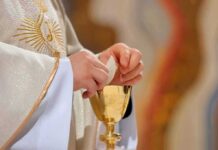 Priest holding a communion wafer over a gold chalice