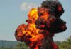 Fireball explosion with thick black smoke in open landscape