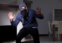 Thief Makes Embarrassing Blunder During Home Burglary Person in hoodie and face covering raising hands indoors