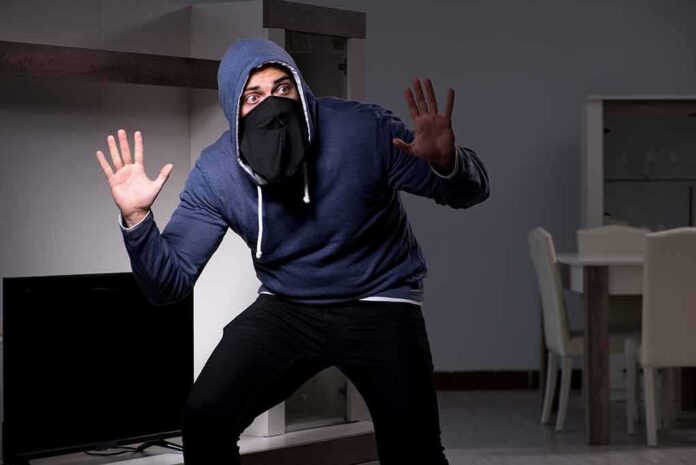 Person in hoodie and face covering raising hands indoors