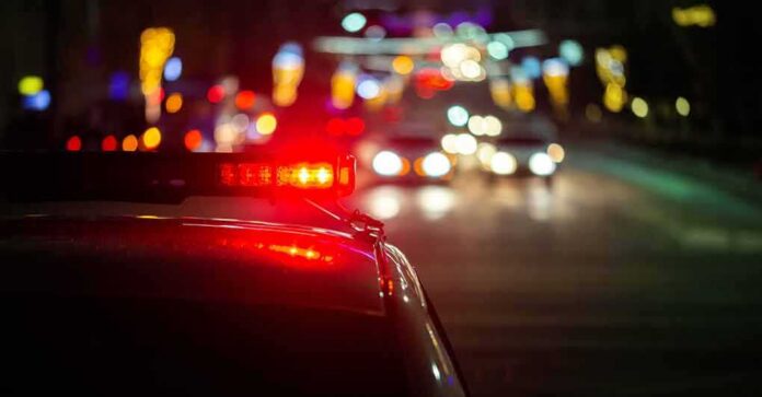 shutterstock_1739802671 Police car with flashing red lights on a city street at night