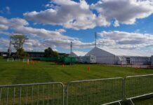 Teen ARRESTED – Gunned Down 12 Outside University Temporary white tents and equipment on a grassy field with traffic cones and metal barriers