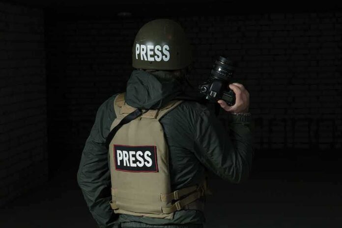 Press photographer in helmet and vest holding a camera