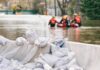 Heroic Reporter Rescues Drowning Man in Flood Sandbags stacked near a flooded street with rescue workers in a boat