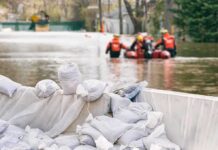 Heroic Reporter Rescues Drowning Man in Flood Sandbags stacked near a flooded street with rescue workers in a boat
