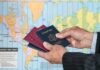 Hands holding multiple passports in front of a world map