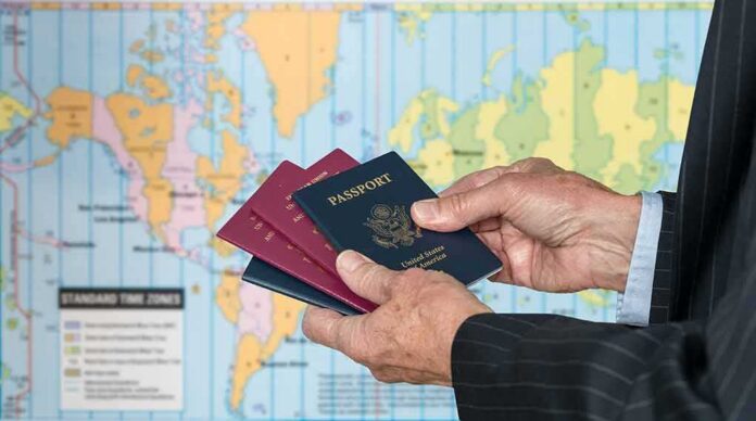 shutterstock_789443080 Hands holding multiple passports in front of a world map